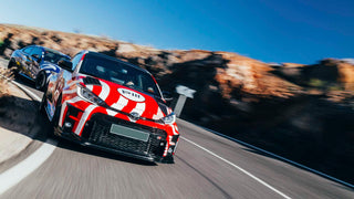 Toyota GR Yaris with a colorful design on a road with mountains in the background, cornering at speed