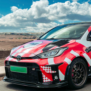Red and white GR Yaris with a unique design by PIRAS Motorsport on a road with a cloudy sky.